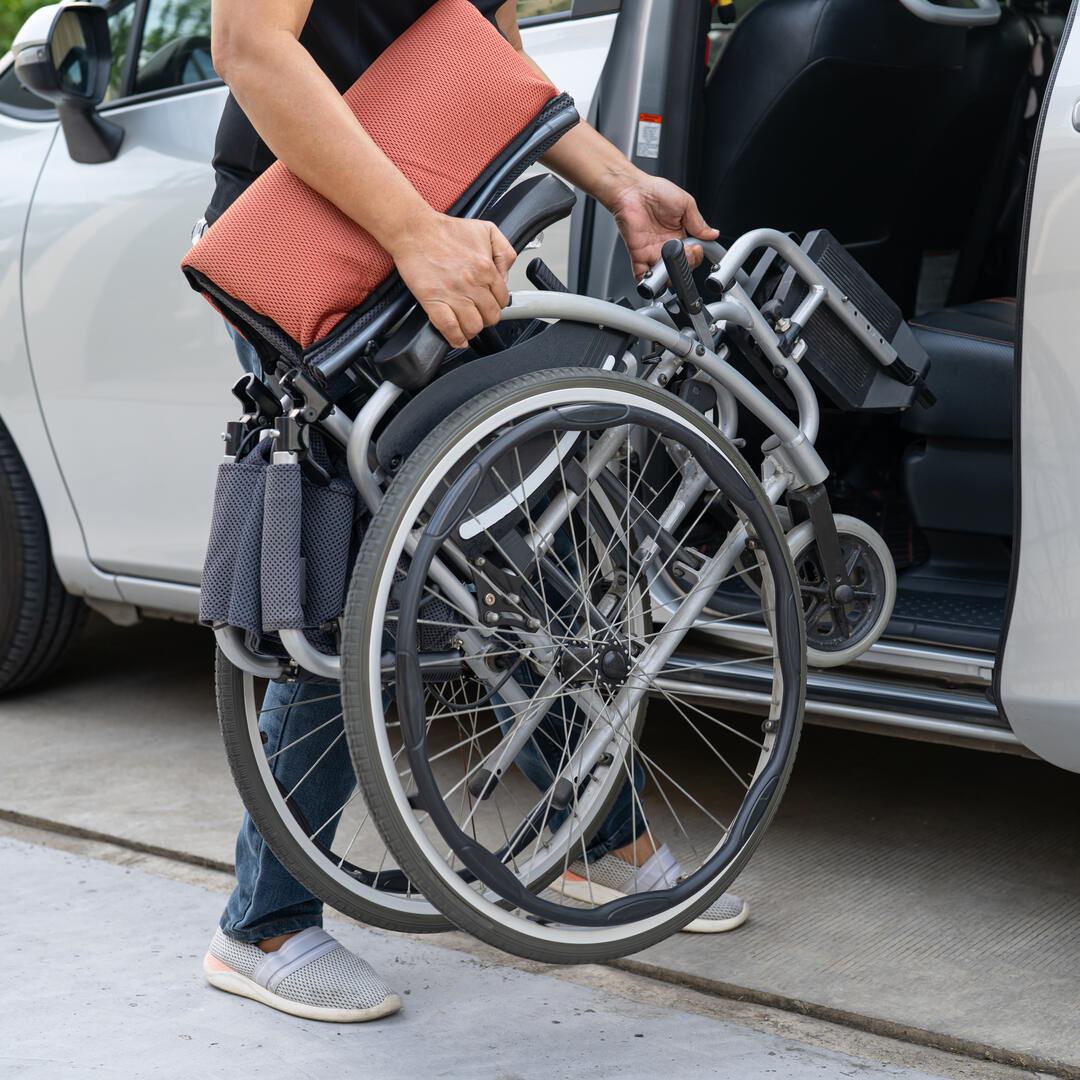 woman loading wheelchair and getting in her car, Accessibility concept.