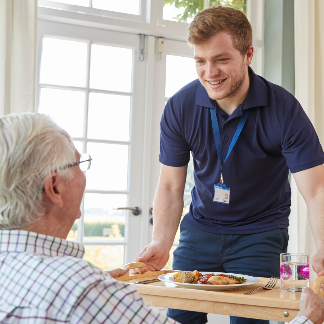 Male care worker serving dinner to a senior man at his home